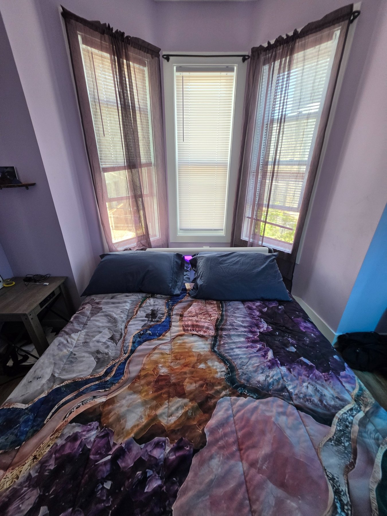Queen bed beneath three windows in the violet room